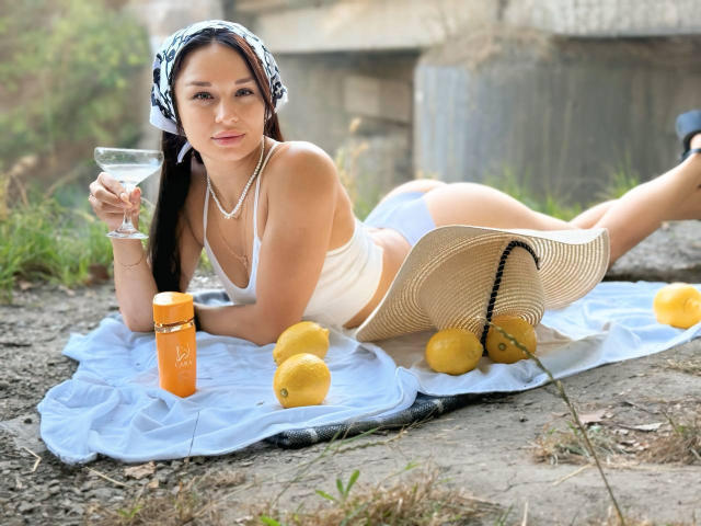 MaryLoveX, laying on a white towel, wearing a white bikini, holding a martini glass, with lemons, a sunhat, and an orange bottle, has a cute face, and small tits.