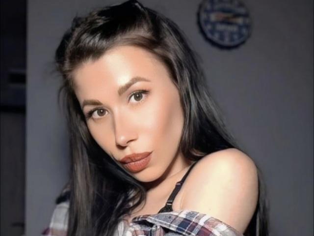 Glidia a les lèvres pulpeuses, les yeux marron et les longs cheveux noirs. Elle porte une chemise à carreaux avec un décolleté sur une épaule, qui révèle ses épaules et ses bretelles noires. Sa peau est claire et lisse..