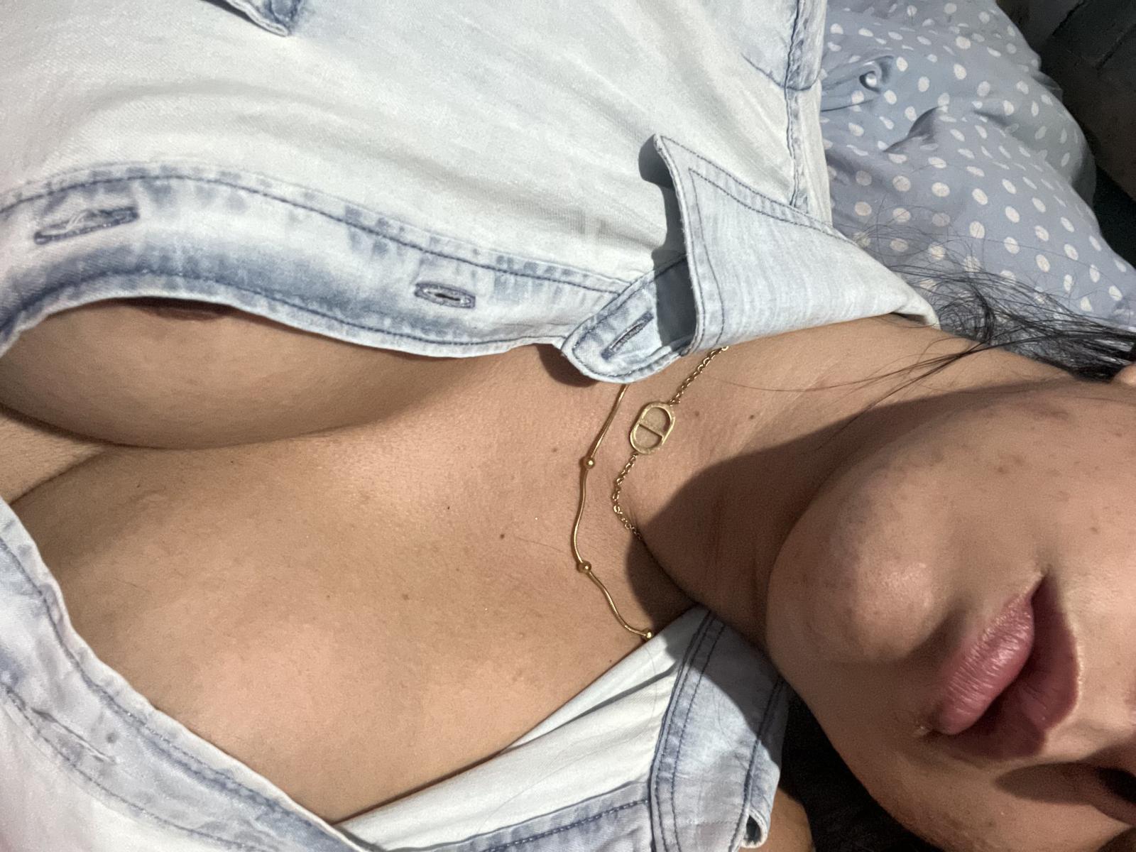 MonahLiza's tits are visible under a white shirt with blue denim sleeves, showing a gold necklace. Her face is partially in the frame with pouty lips.
