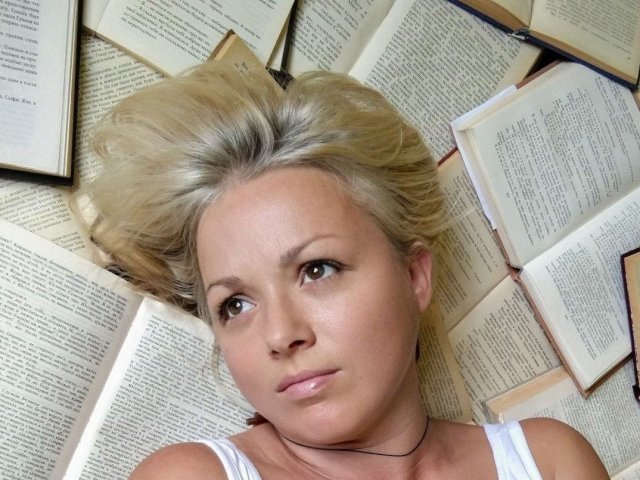 LinsyKim with blonde hair, lying on open books, white tank top, brown eyes, subtle makeup, necklace, books all around, serious expression, slight blush, soft light, relaxed.