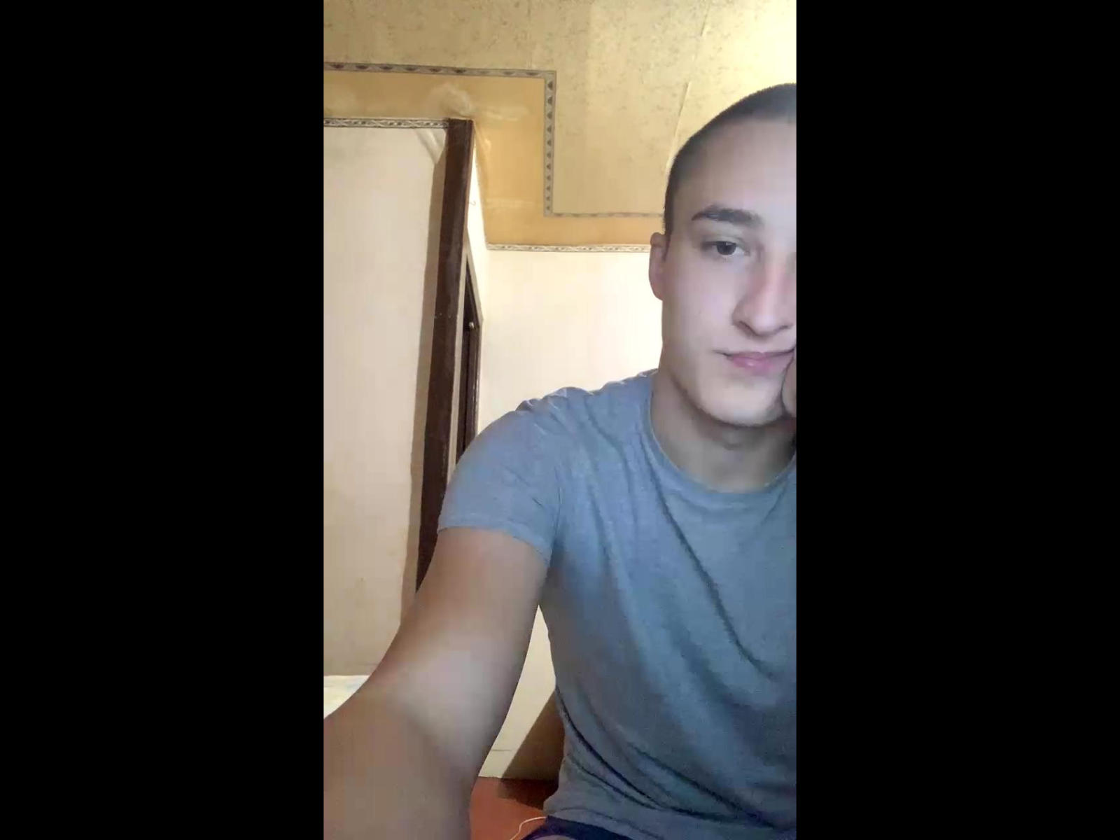 MishaTopp69, con la cabeza rapada, una camiseta gris y una ligera sonrisa, aparece en un selfie parcial con su brazo derecho. Su rostro está ligeramente inclinado hacia la derecha..