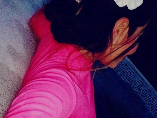 AdamsMerlina lying on her side, wearing a bright pink, form-fitting top, with her dark hair partially covering her face, showing her bare shoulder and ear.