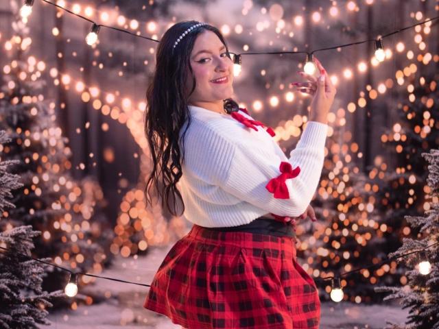 VictoriaRiver with long black hair, white sweater, red plaid skirt, and red bow, smiling, holding string lights, pearl headband, standing in snowy forest, warm lights in background.