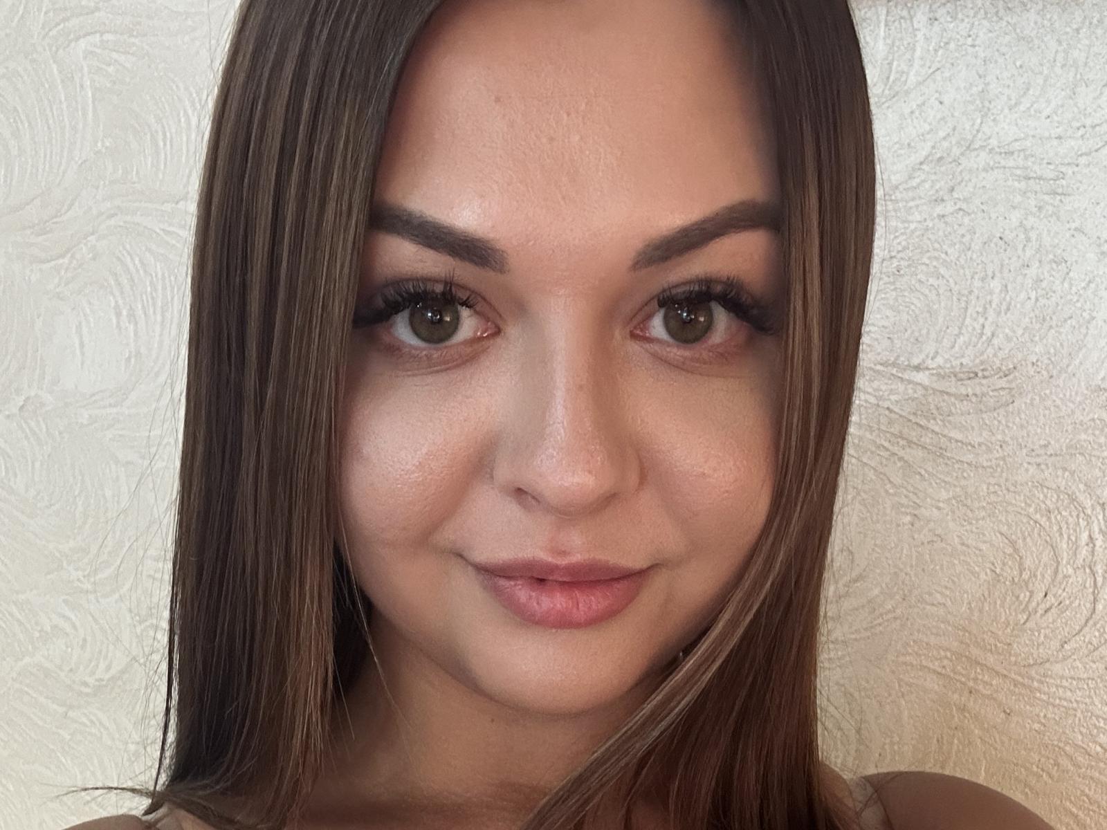 AlisaMilana's face, showing brown eyes, straight brown hair, and a subtle smile, with her eyebrows raised slightly. Her skin is smooth, and she has full, pink lips.