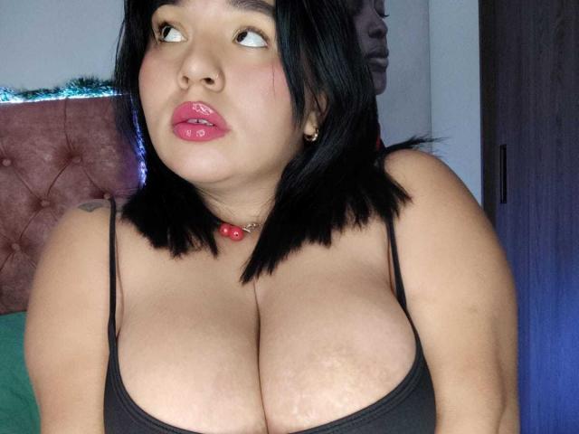 CristinaMendez has big, shiny pink lips, black shoulder-length hair, and large, saggy tits in a black tank top. She's looking to the side with a slightly pouty expression.