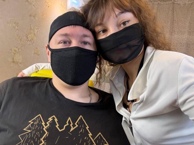 SexLoveHt with curly brown hair and mask, wearing a white zip-up, leans on SexLoveHt in a black beanie and mask, black shirt with mountain design.