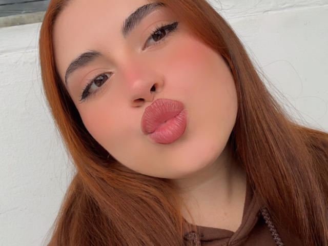 VicluX has pouty pink lips, brown eyes with black eyeliner, and reddish-brown hair. She's making a puffy-lip kiss with a slightly upturned nose.