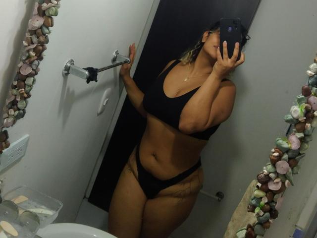MariGonz in a bathroom mirror selfie, wearing black sports bra and thong, showing her tits and ass, holding a phone, tan skin, tattoos on her hip.