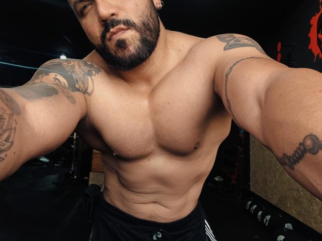 BardoCkroy69, shirtless with a muscular build, tattoos on arms, and a beard, wearing black shorts, taking a selfie, showing his chest and abs.