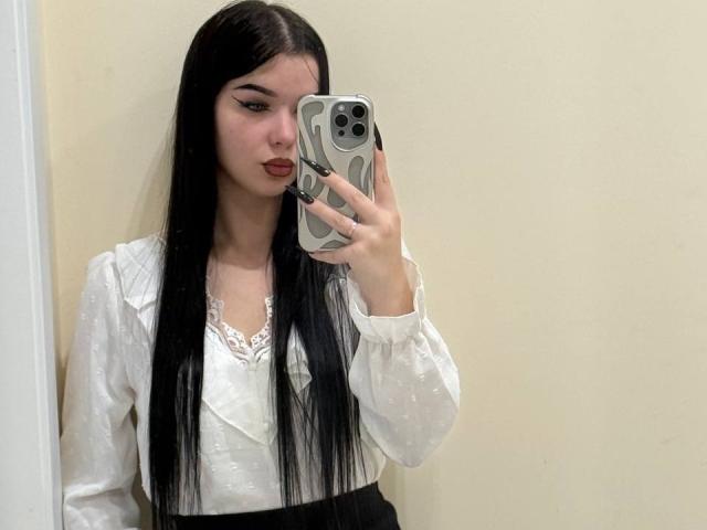 AmberMartha with long black hair, wearing a white lace-trimmed shirt, holding a phone in front of her face, pouting with red lipstick, in a mirror selfie.