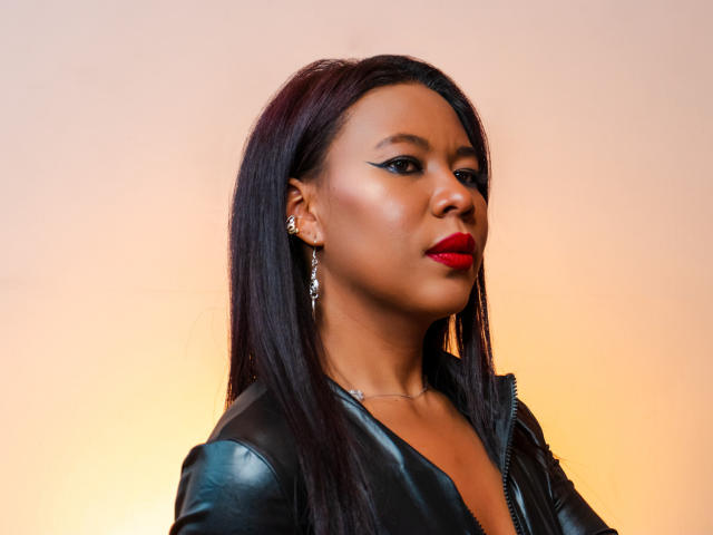  AlexandraSawyer with dark straight hair, red lipstick, black leather jacket, and silver earrings, looking to the side with a confident expression. Sheer, smooth, and stylish.