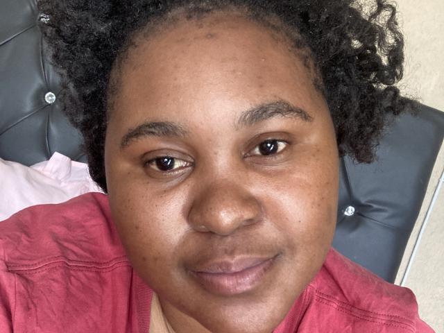 CharmainPhilly69 has a medium brown skin tone, curly black hair, dark brown eyes, and is wearing a red shirt. She's smiling slightly with a nose piercing.