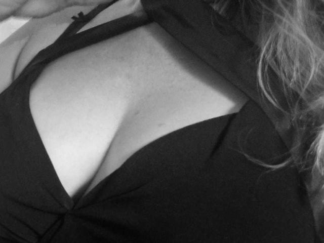 DevilsAngel's schwarzes Oberteil ist heruntergezogen, wodurch ihre großen, weichen, nackten Brüste sichtbar werden. Ihre helle Haut und ihr welliges Haar sind teilweise zu sehen. Das Bild ist ein Schwarz-Weiß-Foto..