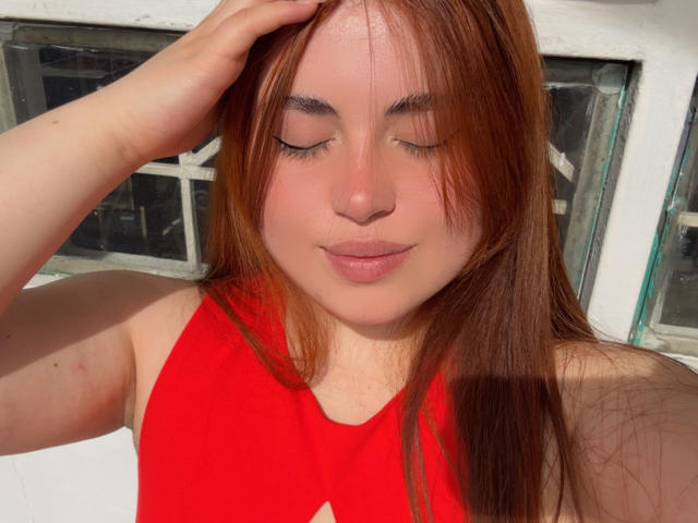 VicluX has red hair, closed eyes, and pink lips, wearing a red halter top, with her hand touching her head, showing a relaxed, pretty face.