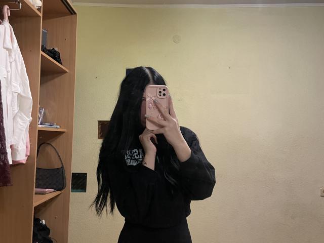 AmaiRin with long black hair, wearing a black long-sleeve shirt and black pants, taking a mirror selfie with her phone, covering her face. Her ass is not visible.