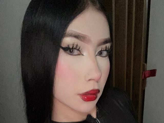 BellaDalthon with long black hair, red lipstick, and winged eyeliner. She has pink blush, black eyelashes, and a nose ring. Her lips are glossy and plump.