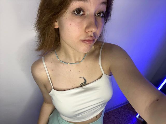 RikkiTikki-hot with light skin, brown eyes, and short brown hair, wearing a white crop top, showing small tits and a crescent moon tattoo, in a selfie.