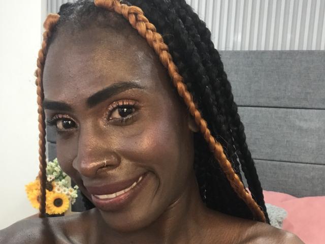 SamaraaJackson69 has dark brown skin, black braided hair with orange tips, a nose ring, and is smiling with brown eyes and glossy lips. Her tits are not visible.
