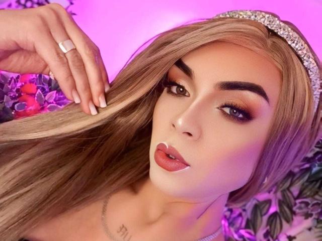 KarolElegance has long blonde hair, a jeweled headband, and full pink lips. She's looking at the camera with brown eyes, wearing a silver ring on her left hand.