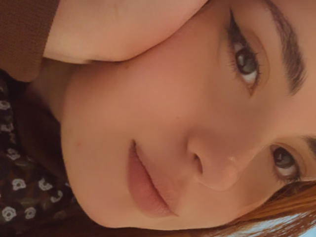 VicluX has a cute face with brown eyes, thin eyebrows, and slightly parted pink lips. Her right arm is resting on her cheek. She has light skin and red hair.