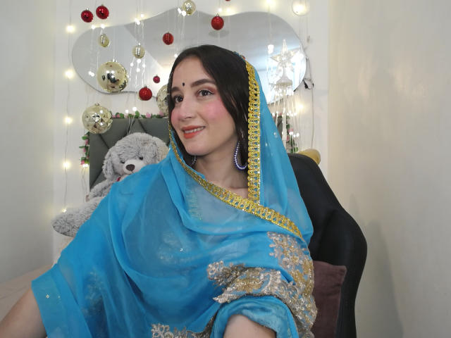 JalimaMona in a blue saree with gold and silver embroidery, purple earrings, smiling, dark hair, pink blush, and a small red bindi, holding a fluffy gray teddy.