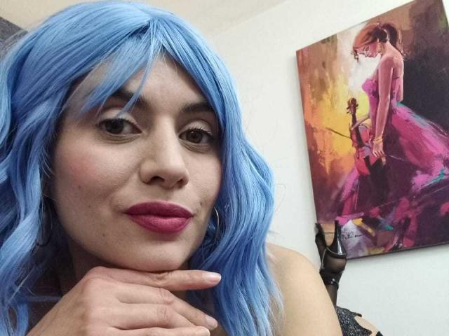 Lilaa, een vrouw met blauw haar, roze lippenstift en oorringen, leunt haar kin op haar hand en laat haar schattige gezicht en zachte glimlach zien. Een schilderij van een vrouw in roze..