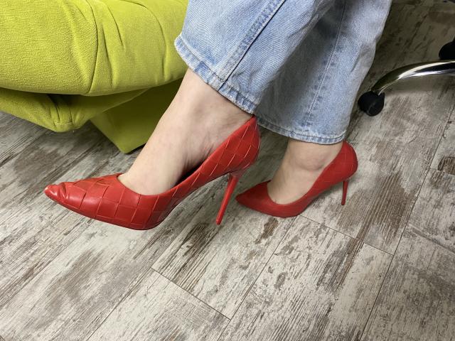 Karpinka's feet in red, pointy, high-heel shoes with a crocodile pattern. She's wearing light blue, slightly frayed jeans. The shoes have red heels and a shiny finish.