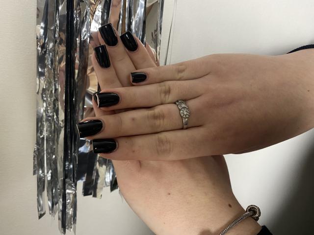 Karpinka's hand with shiny black nail polish, a silver ring on her ring finger, and a bracelet on her wrist. Her fingers are slightly curled, showing off her nails.