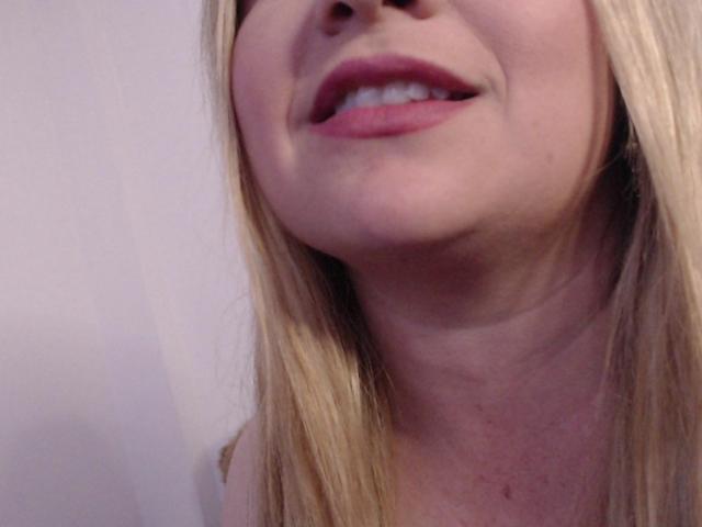 NatalyHami's face with blonde hair, slightly open pink lips showing white teeth, and a light skin tone. Her nose is partially visible, and the shot is a close-up.