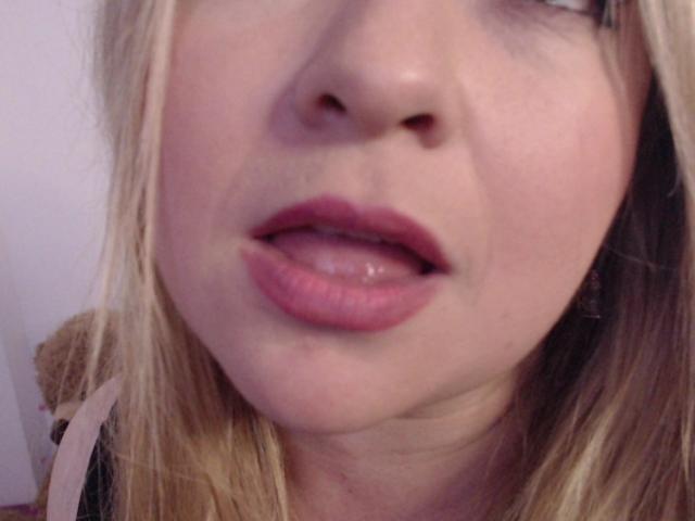 NatalyHami's face, showing her pink lips and slightly parted tongue, with blonde hair and a subtle nose. Her eyes are partially visible, and she's wearing pink lipstick.