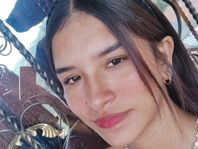 ImmyAllison has dark brown hair, a small nose ring, and earrings, with pink lipstick and a slight smile, looking at the camera with brown eyes.