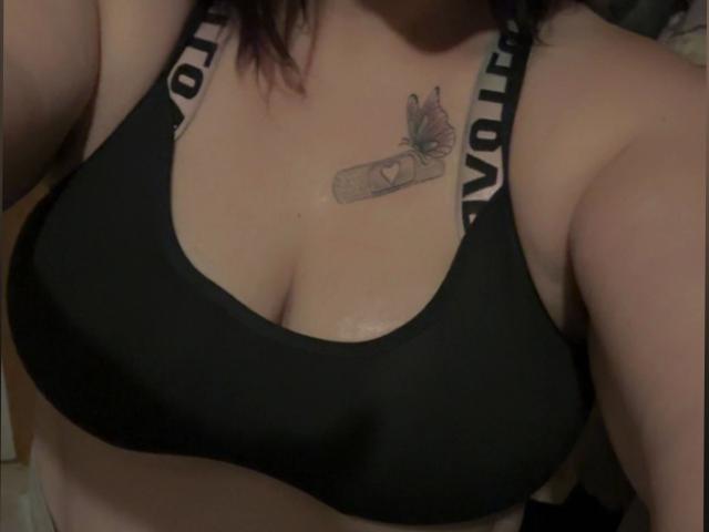 Siindyxx-hot's black sports bra, showing her tits, with a tattoo of a book and butterfly on her chest. She's got white straps with "NOR" on them.
