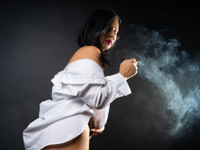 MonicaVixen with black hair, off-shoulder white shirt, exposing her ass, smoking, blue smoke rising from her hand, dark background, red lipstick, confident, sexy, subtle light.