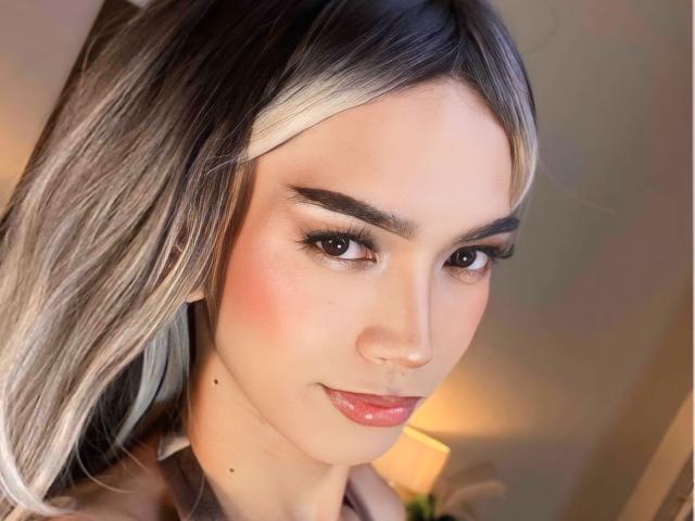 AmandaMooree has long, straight, black-and-silver hair, brown eyes, and a cute smile with pink lipstick. She's got a few small moles on her face and subtle eyeliner.