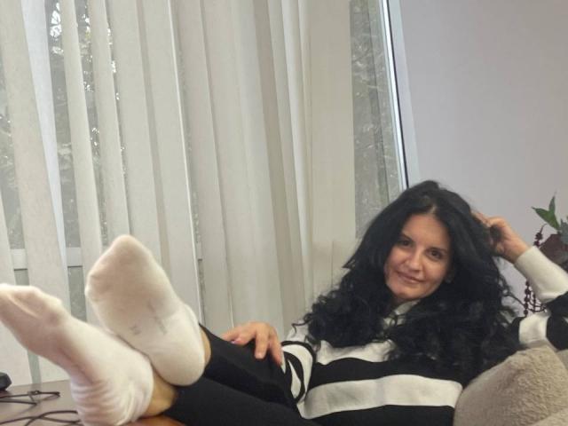 Marlinaa with curly black hair, smiling, wearing a black and white striped sweater, and white socks, has her legs up, showing her cute ass, in a relaxed pose.