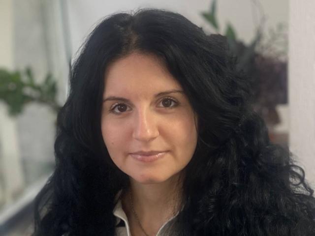 Marlinaa has long, wavy black hair, brown eyes, and a slight smile. She's wearing a gray shirt with a white collar. Her nose is slightly upturned.