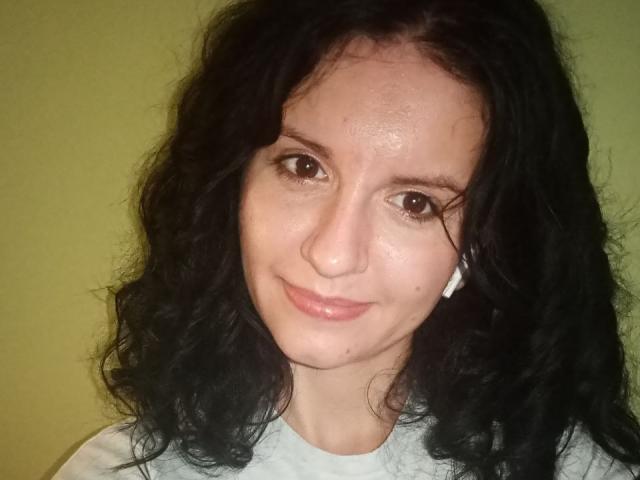 Marlinaa has curly black hair, brown eyes, light skin, and is smiling with a small nose and slight pink lips. She's wearing a white shirt with a small white earpiece.