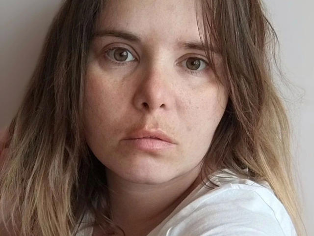ElenaSchatz-hot has a serious face with brown eyes, slightly parted lips, and messy brown hair. She's wearing a white shirt, looking straight at the camera.