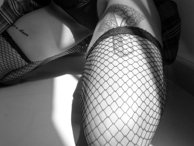 AnneeFoxy's ass in black fishnet stockings, tattoo on upper thigh, reflected in mirror, shadow on floor, bare skin, subtle light, monochrome, intimate, close-up.