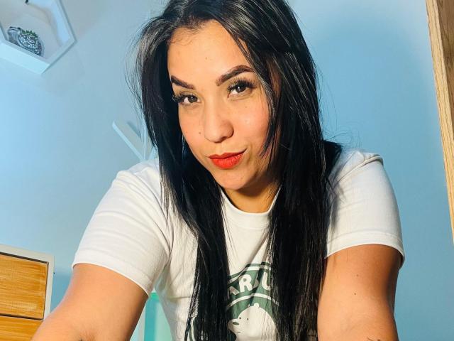 SalomeMilleer with long black hair, wearing a white T-shirt, red lipstick, and a slight smile, showing her face and upper chest, looking at the camera.