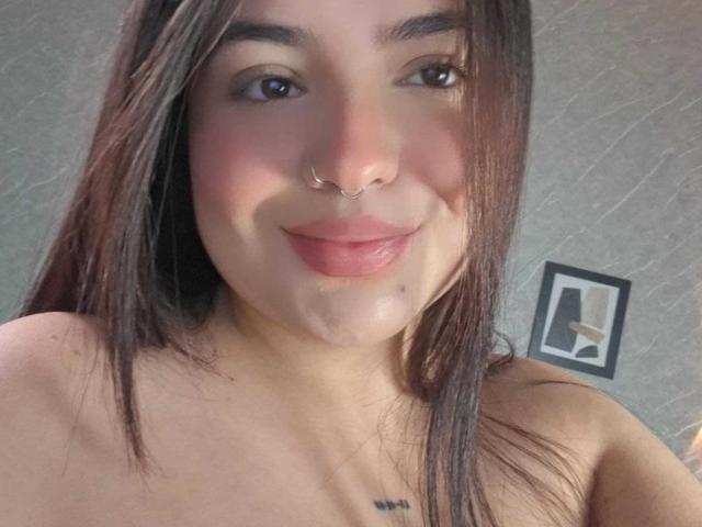 ValeriJoness with straight brown hair, nose ring, and subtle smile, showing a small tattoo below her bare shoulders, and a visible wet spot on her chest.