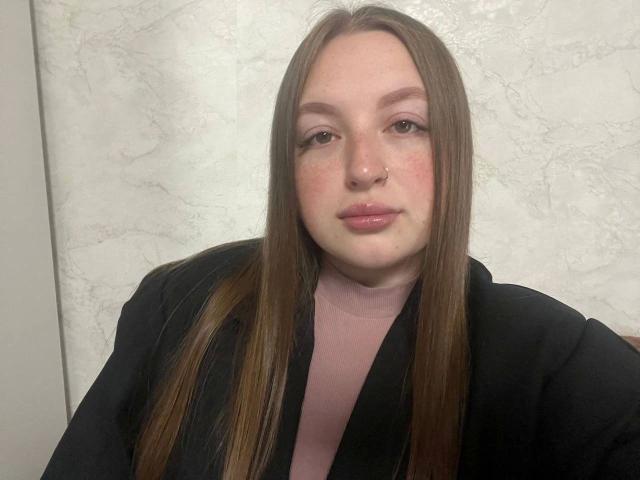GirlPlayer-hot with straight brown hair, nose ring, pink turtleneck, black robe, and subtle makeup, looking slightly pouty.