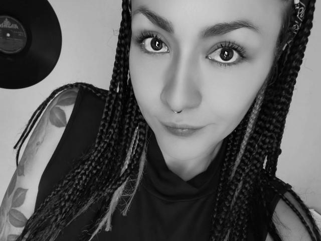 Black-and-white selfie of AlejadArte with braided hair, nose ring, and tattoos on her arm. She's looking at the camera with a slight smile, showing her eyes and lips.