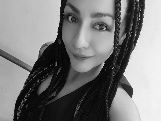Black-and-white photo of AlejadArte with long braids, hoop earrings, and a slight smile. AlejadArte's eyes are focused, and she's wearing a sleeveless top.