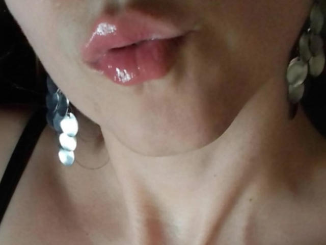 ImFireMoon's glossy pink lips are slightly parted, showing a bit of her upper teeth. She has shiny earrings with white round stones and a black strap on her shoulder.