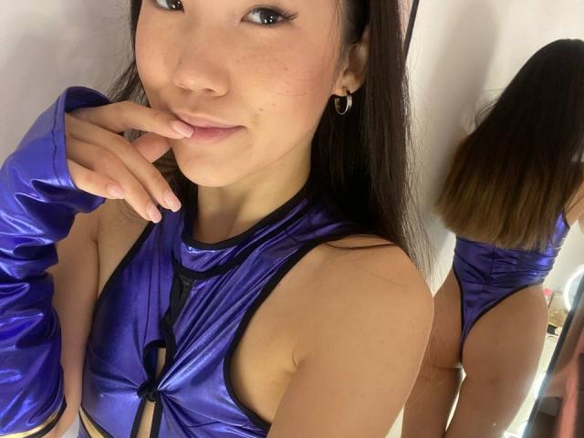DivineMadness with long brown hair, wearing a shiny blue halter top and matching arm sleeves, touching her lips, showing her ass in a mirror reflection.