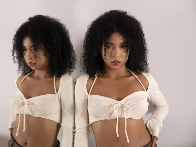 IvyRoberts with curly black hair, wearing a white crop top with tied front, revealing her small tits and flat stomach, standing in front of a mirror.