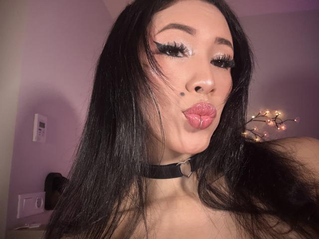 Nashiro Sakurai, com longos cabelos pretos, usando um colar preto, com lábios rosados e brilhantes, e cílios grossos, tem uma pequena marca de beleza na bochecha direita..