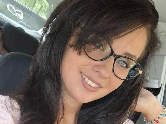 CuteLexy-hot with black glasses, smiling, wearing pink shirt, has long dark hair, blue eyes, and light skin, seated in car. Boobs not visible. Ass not visible. Pussy not visible.