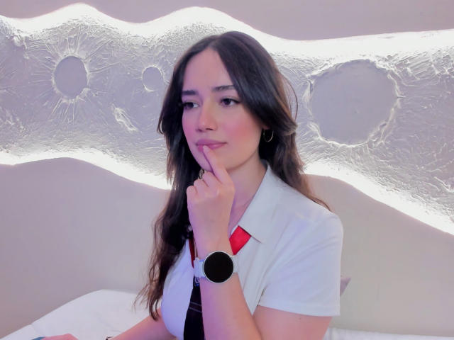 MariaLoft met donker haar, een wit shirt, een rode kraag, een zwarte stropdas, een vinger op haar lippen, een zwarte polsband, die subtiel glimlacht, een golvende muur op de achtergrond, roze verlichting, schattig, sexy..